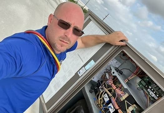 An Air Star Now technician with a rooftop unit's control panel open